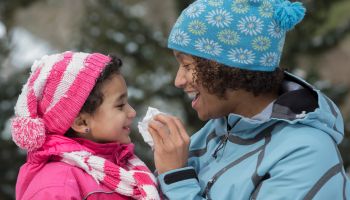 Mother wiping daughter's nose in snow outdoors