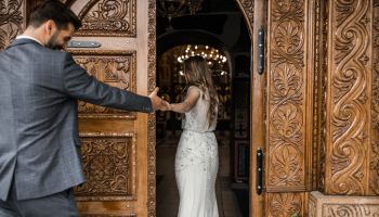 Groom and bride holding hands and entering in church, back view