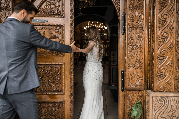 Groom and bride holding hands and entering in church, back view